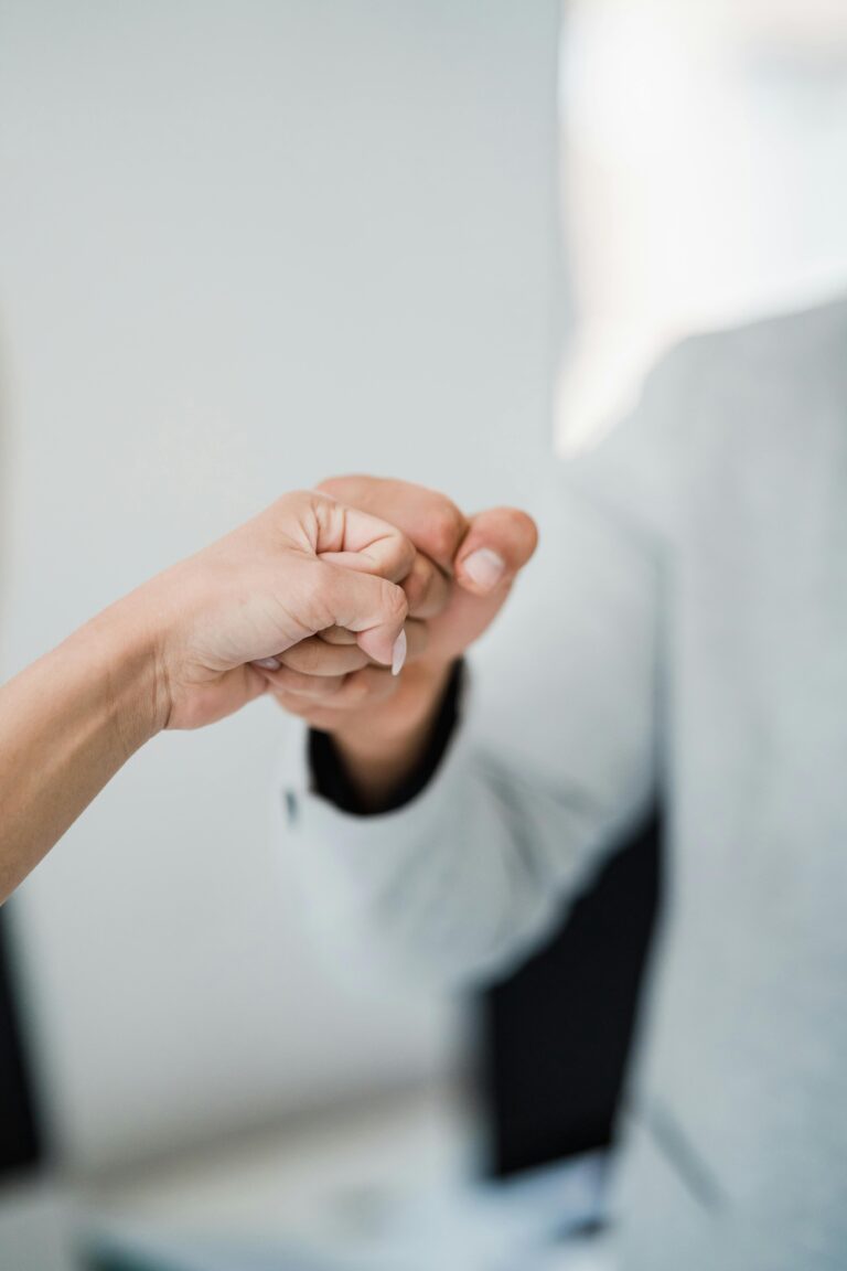 Close-up of two professionals bumping fists, symbolizing teamwork and respect in a modern office.